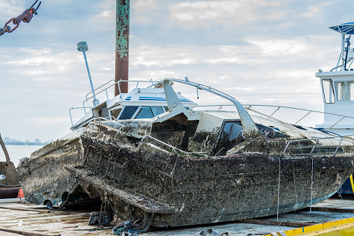 Environmental authorities removing abandoned boats sunk at sea with a crane. These boats pollute the waters and endanger marine fauna.