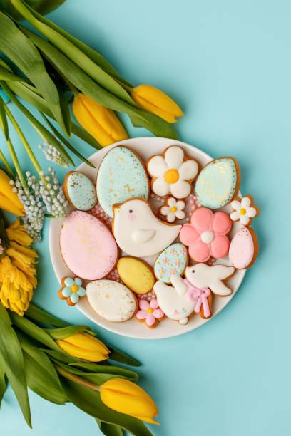 istock Easter greeting card with fresh tulip flowers, Gingerbread cookies - Easter eggs, bird, bunny and flowers on white plate, top view with copy space, homemade sweets for seasonal spring party 1302714653