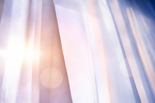 Translucent curtain background at sunrise with mellow pastel colors and soft lens flare.