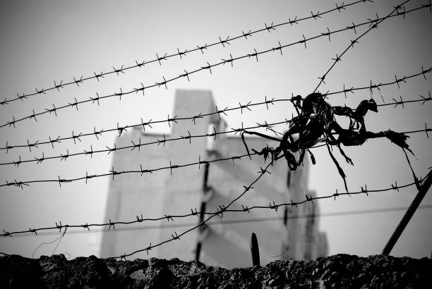 istock Barbed wire stretched over the wall with a multistory building seen far away in blur. 1302736532