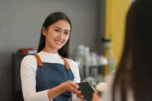istock Barista with apron holding over smartphone to help customer pay for purchase a coffee 1302737522
