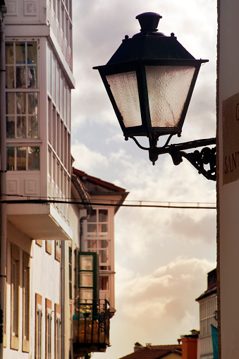 Retro style street light, traditional galerías in narrow street and detail of facades in old town at dusk.  A Coruña, Galicia, Spain.