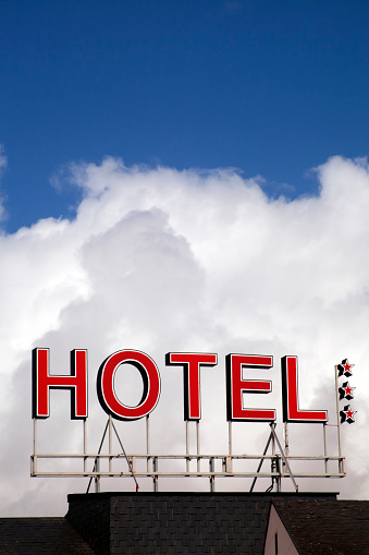 Large hotel sign on top of building, slate rooftop and three stars symbol , clear sky and clouds in the background.