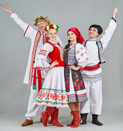 A group of dancers different age are dressed in paired (female and male) Belarus and Moldova traditional clothes. They are posing together, smiling looking at the camera. Studio shooting