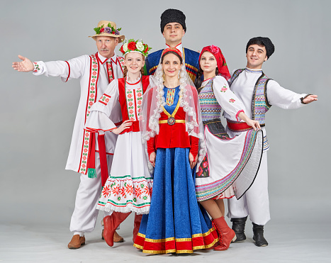 A group of dancers different age are dressed in paired (female and male) Belarusian, Georgian and Moldavian traditional clothes. They are posing together, smiling looking at the camera. Studio shooting
