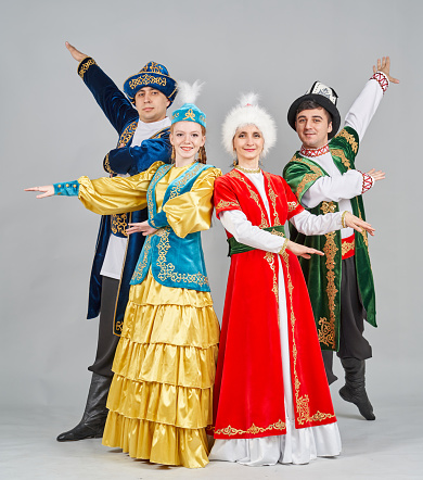A group of dancers (teenage girl, two young men and middle-aged woman) are dressed in paired (female and male) Kazakh and Kyrgyz traditional clothes. They are posing together, smiling looking at the camera. Studio shooting