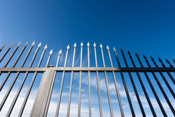 wrought iron gate with sharp points on blue sky with clouds - iron gate imagens e fotografias de stock