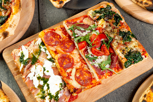 Pizza romana square slices with various ingredients on wooden board