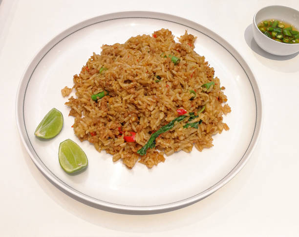 istock rice topped with stir fried pork and basilon white plate serving with chilli and fish sauce on table. Isolated white background 1302750659