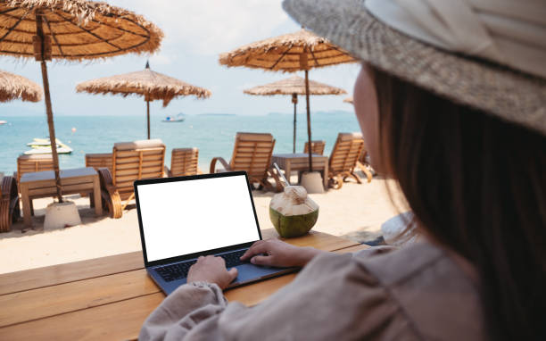 istock a woman using and typing on laptop computer with blank desktop screen while sitting on the beach 1302754524