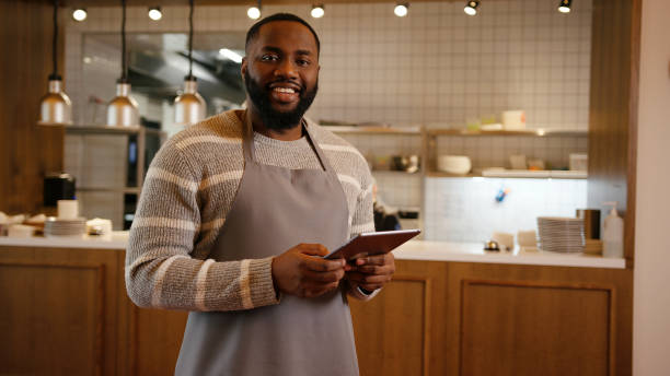 dueño afroamericano de pequeña empresa sostiene tableta en acogedor restaurante - cardigan men african ethnicity african descent fotografías e imágenes de stock