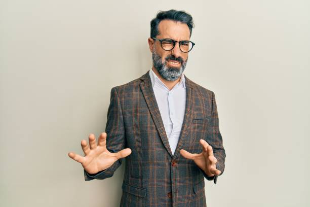 Middle age man with beard and grey hair wearing business jacket and glasses disgusted expression, displeased and fearful doing disgust face because aversion reaction. with hands raised Middle age man with beard and grey hair wearing business jacket and glasses disgusted expression, displeased and fearful doing disgust face because aversion reaction. with hands raised disgust stock pictures, royalty-free photos & images