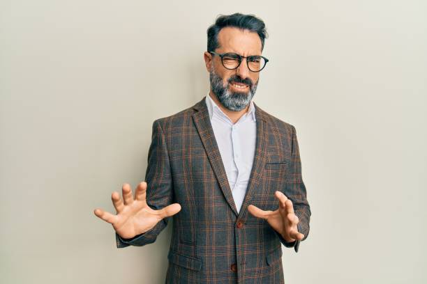 middle age man with beard and grey hair wearing business jacket and glasses disgusted expression, displeased and fearful doing disgust face because aversion reaction. with hands raised - offense imagens e fotografias de stock