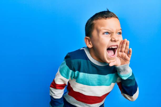 ストライプのセーターを着た小さな子供の男の子が叫び、口の上に手を置いて大声で叫んでいます。コミュニケーションの概念。 - one little boy audio ストックフォトと画像