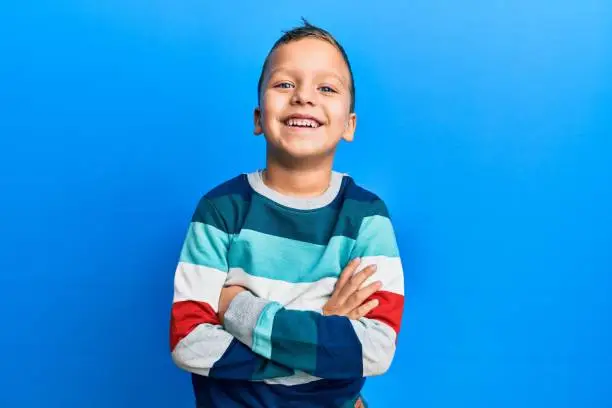 Little kid boy wearing striped sweater happy face smiling with crossed arms looking at the camera. positive person.