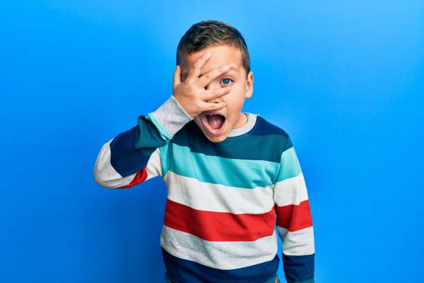 kleines kind junge trägt gestreiften pullover guckt in schock decken gesicht und augen mit der hand, blick durch die finger angst - hand over head stock-fotos und bilder