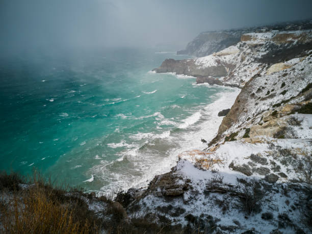 A snow storm covered the seashore. Bright turquoise sea, squally wind, huge waves, bright sun. The concept of bad weather, cold, sudden arrival of winter. Cape Fiolent Sevastopol Crimea top view