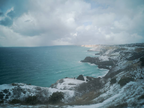 A snow storm covered the seashore. Bright turquoise sea, squally wind, huge waves, cloudy sky. The concept of bad weather, cold, sudden arrival of winter. Cape Fiolent Sevastopol Crimea top view