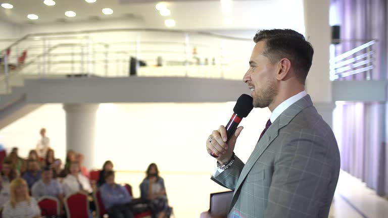 Speaker giving a talk on corporate Business Conference. Audience at the conference hall. Business event. A young man in suit presenting a business seminar. Coach Business People Meeting Office Training Concept