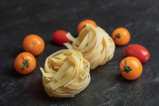 Uncooked nest pasta with cherry tomatoes on a dark background