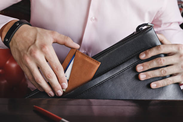 A business man puts a leather wallet in a briefcase