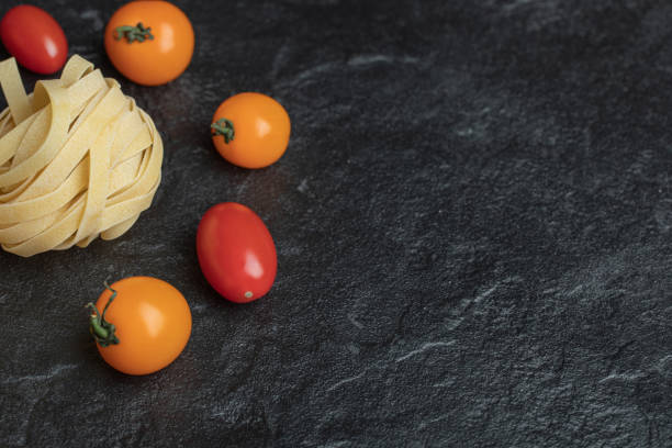 Uncooked nest pasta with cherry tomatoes on a dark background
