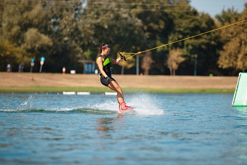 Young woman in wetsuit finishing ride on wakeboard and holding towing rope with one hand