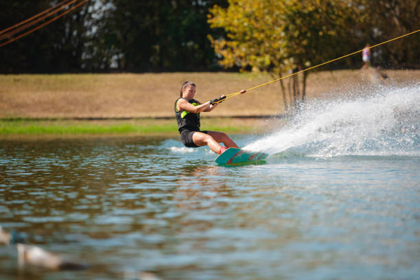 istock Young woman in wetsuit riding wakeboard pulled by towing rope and splashing 1302760516