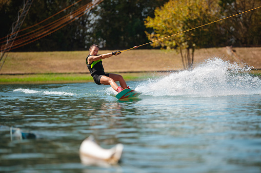 Young woman in wetsuit riding on water surface pulled by towing rope, reclining a splashing