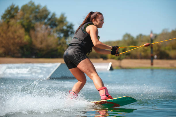 istock Smiling young woman on wakeboard making a splash on lake surface 1302760547