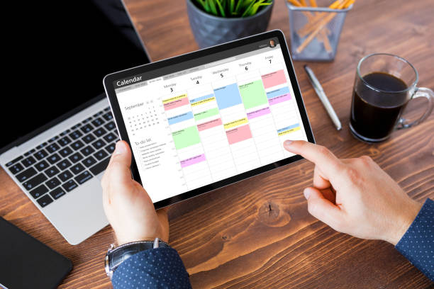 職場でタブレットでカレンダーアプリを使用する男性 - busy schedule ストックフォトと画像