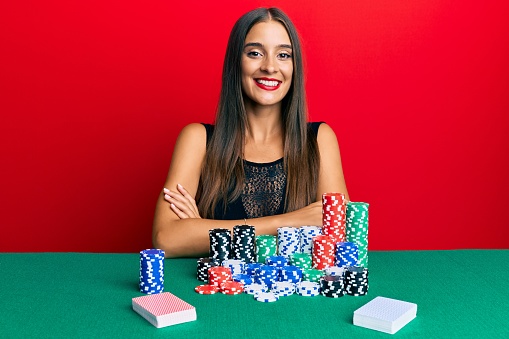 Young hispanic woman sitting on the table playing poker happy face smiling with crossed arms looking at the camera. positive person.