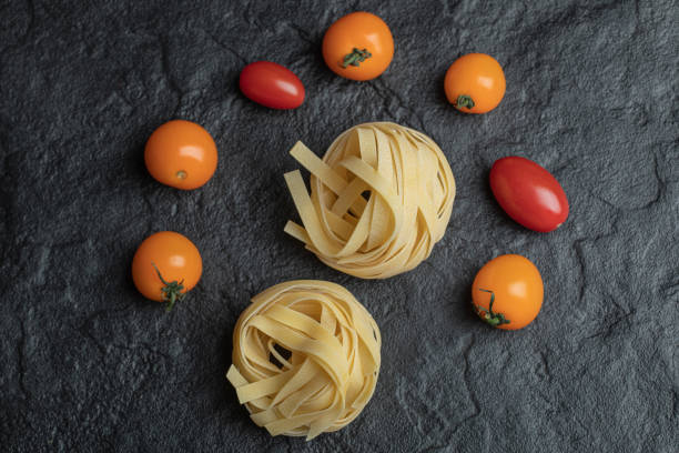 Uncooked nest pasta with cherry tomatoes on a dark background
