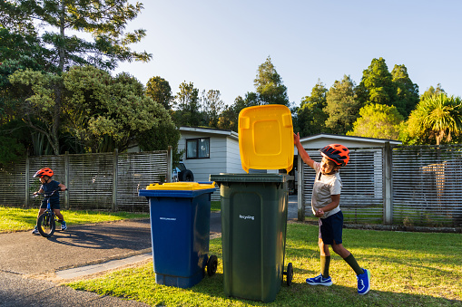 Kid with the bike helmet on throwing the recyclable cardboard boxes in recyclable bin in Auckland, New Zealand.
