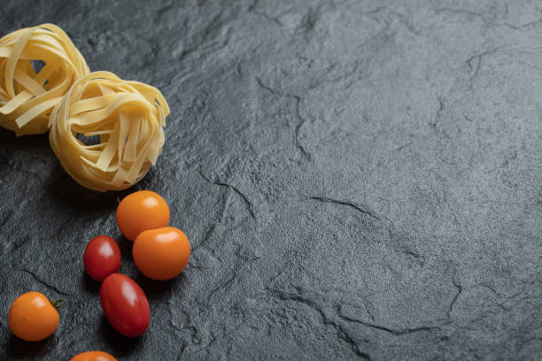 Uncooked nest pasta with cherry tomatoes on a dark background