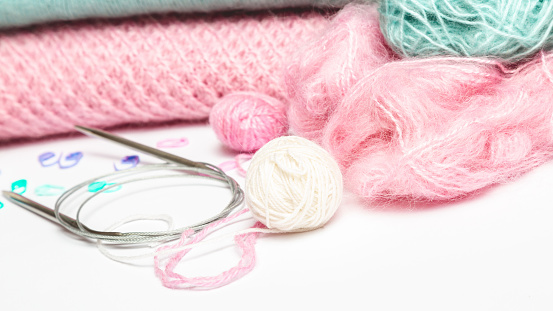 Accessories for knitting. Knitted from pink yarn sweater and threads for knitting close-up on a white background.Copy space. Top view, needlework concept.