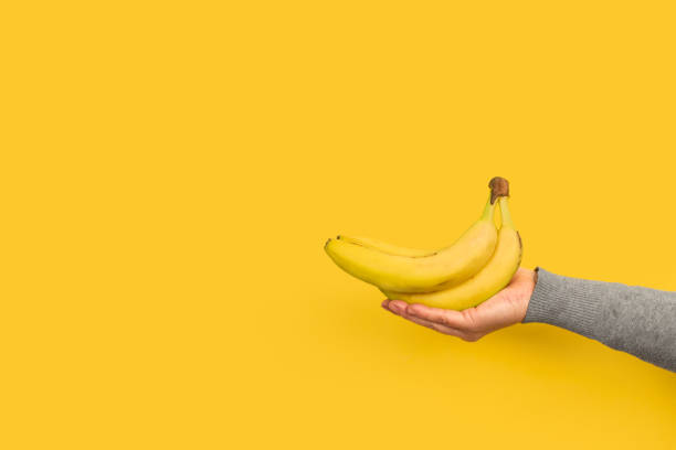 istock Woman hand holding bananas on a yellow background 1302766473