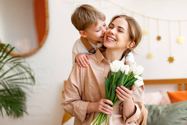 tender son kisses the happy mother and gives her a bouquet of tulips, congratulating her on mother's day - mothers day flower gift bouquet imagens e fotografias de stock