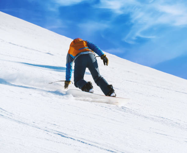 istock Snowboarder riding down a steep slope on a sunny day with clear blue skies. 1302771835