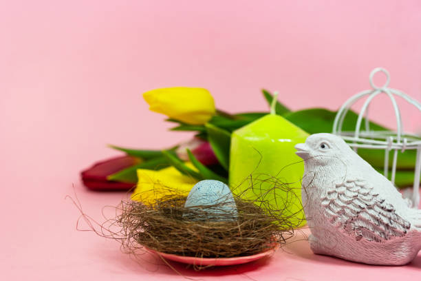istock Spring postcard. Easter eggs in a nest with moss, a bird, a cage and a bouquet of fresh tulips, a green candle on a pink background. Easter concept. Flat top view copy space. Spring flowers tulips. 1302771965