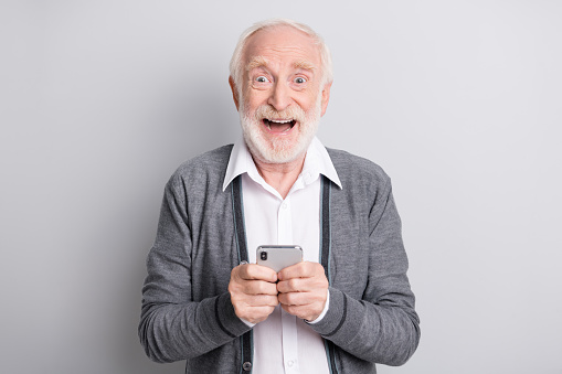 Portrait of old white hair hooray man hold telephone wear dark sweater isolated on grey background.