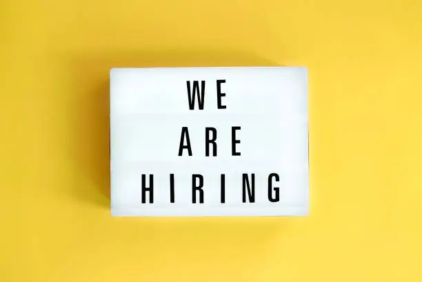 Lightbox with a words text We Are Hiring board on yellow background. Surviving economical and financial crisis. Job seeking, recruiting and business concept.