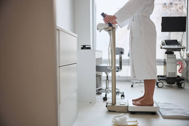 istock Barefoot Caucasian lady in a bathrobe measuring her body weight 1302776287