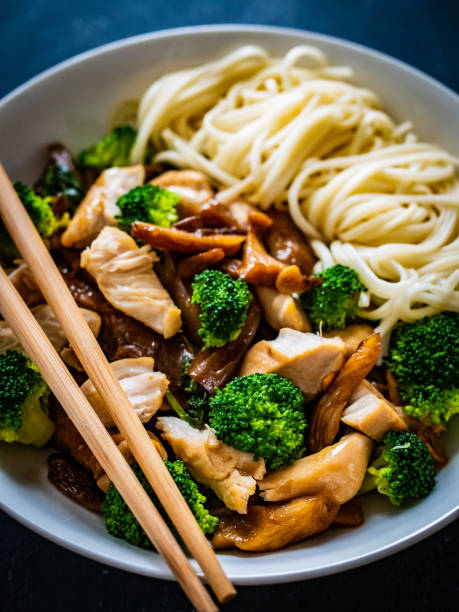 Noodles with chicken nuggets, oyster mushrooms and broccoli on black table