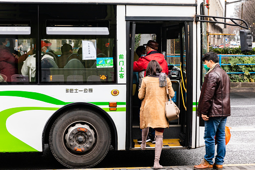 Shanghai, China - February 17, 2021: People with face masks boarding the electric bus in the front door in Hongkou District, Shanghai.
