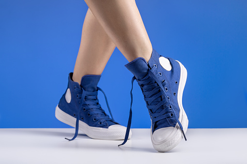 A pair of blue sneakers with laces on women's legs. Shoes for sports and travel.