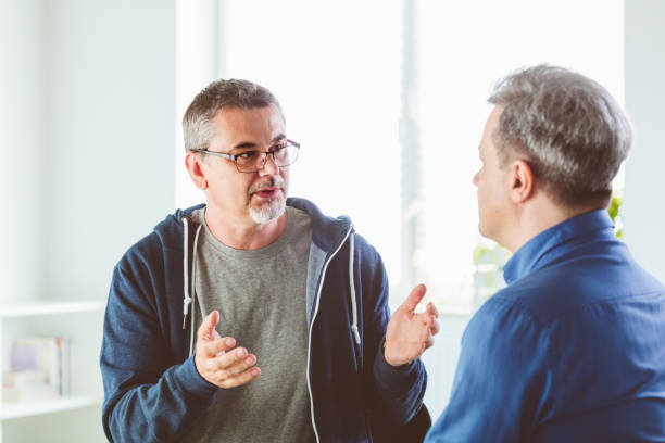Mature psychotherapist talking with depressed man. Coach is discussing about mental illness with man. They are in meeting in psychotherapeutic office.