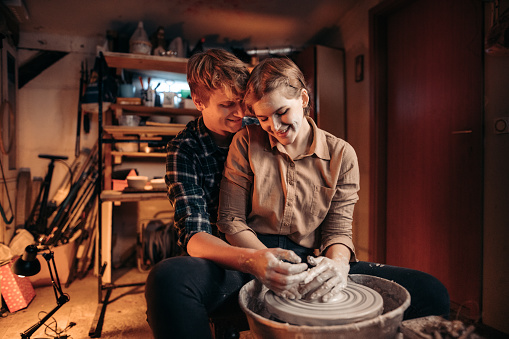 Couple romancing and working on pottery wheel at workshop