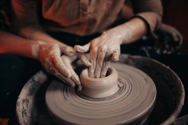 Couple together shaping clay bowl on pottery wheel at workshop