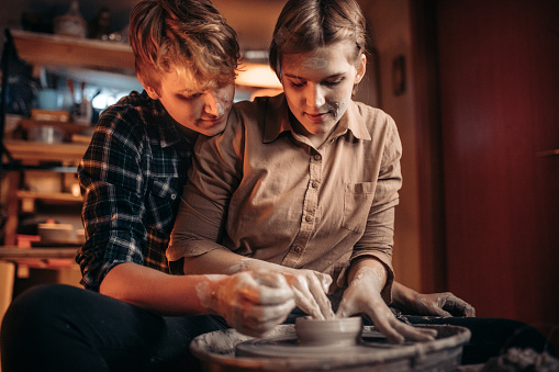 Couple making clay bowl in pottery wheel at workshop
